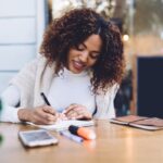 A remote nonprofit worker working at an outdoor table and writing in a notebook.