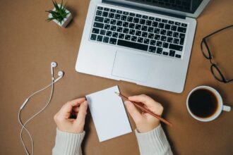 A woman working on updating her resume, using a laptop and writing in a notepad.