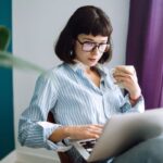 A woman working from home on a laptop and holding a cup of coffee.