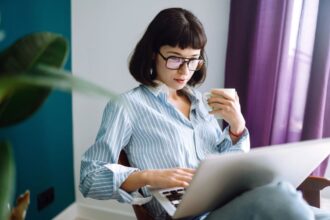 A woman working from home on a laptop and holding a cup of coffee.