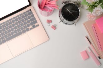 Overhead view of a remote worker's desk, with a laptop, pencils, notebooks, and clock.