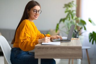 A woman with ADHD working at home using a laptop and writing in a notebook.