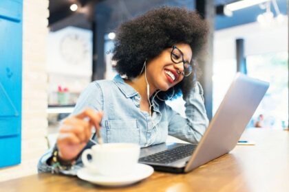 A woman working remotely from a cafe, using a laptop and drinking coffee.